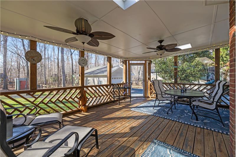 Expansive screened porch with wood plank flooring, ceiling fans, skylights extends the home's living and entertaining space.