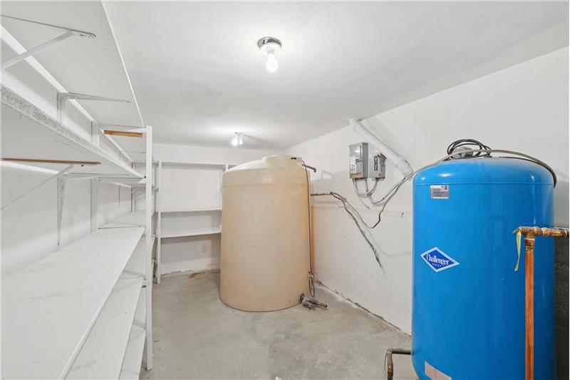 Storage room in basement has unused cistern tank and blue well tank. Hot water sidearm to the boiler is off-camera to right