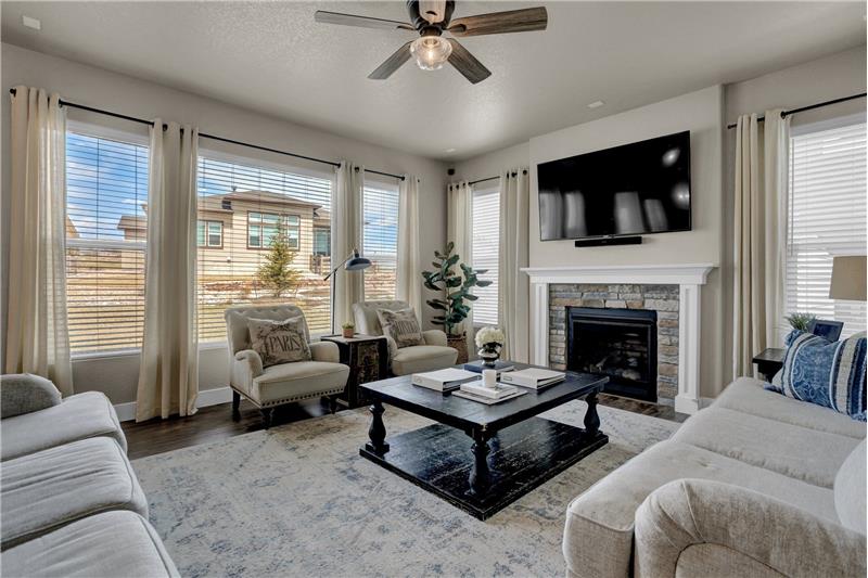 Great Room with Lighted Ceiling fan, Wall of Windows, & Gas-Log Fireplace with Stone Surround