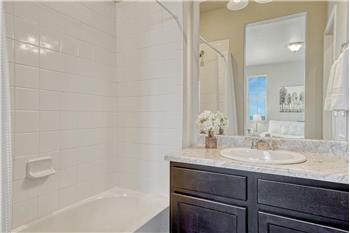 The upper level Primary Bathroom boasts a vanity, mirror, and tiled tub/shower.