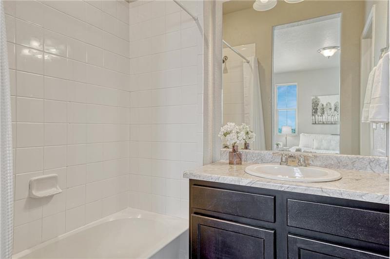The upper level Primary Bathroom boasts a vanity, mirror, and tiled tub/shower.