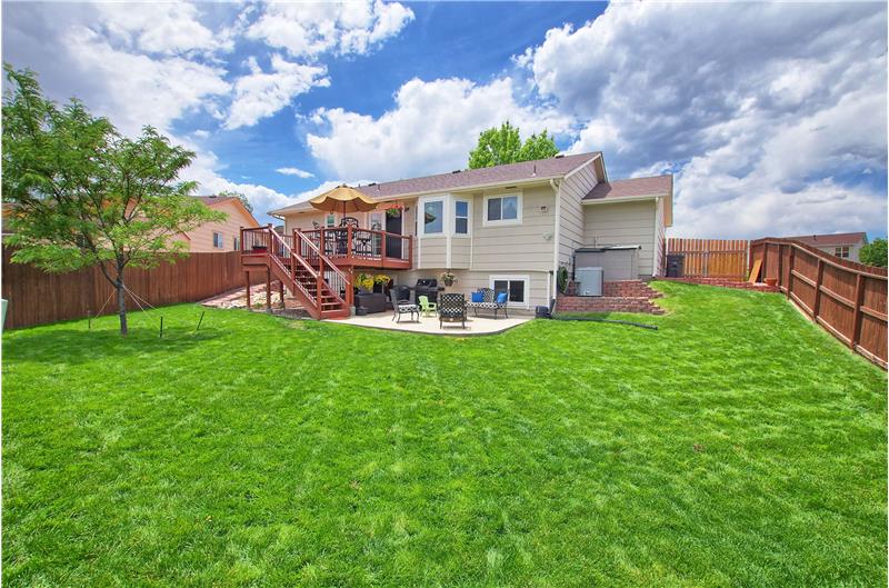 Large, fenced backyard with storage shed, deck, and patio