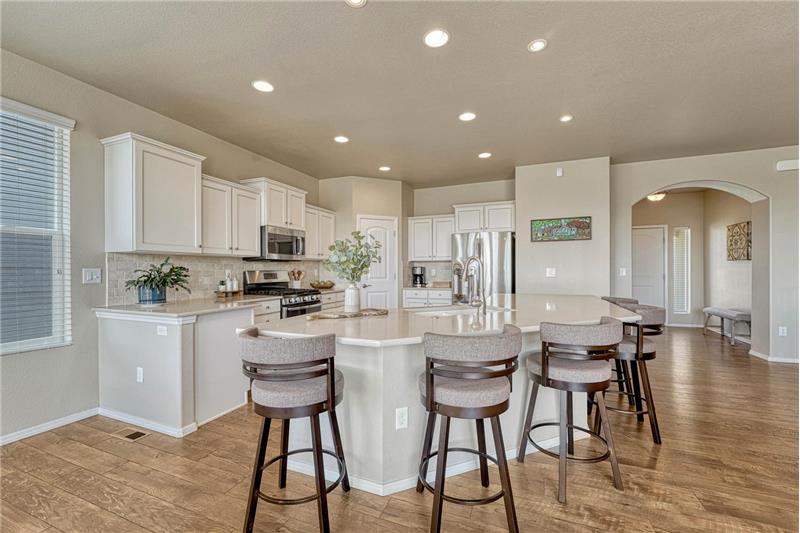 Gourmet Island Kitchen with pantry, white cabinetry with quartz countertops, a breakfast bar, and stainless steel appliances.