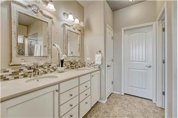 Primary Bathroom with tile flooring, a dual sink quartz vanity, framed mirrors, and tiled shower with built-in seat.