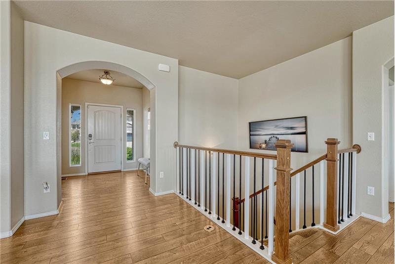 Interior front foyer with gleaming LVP flooring and wood and iron rails to the finished basement.
