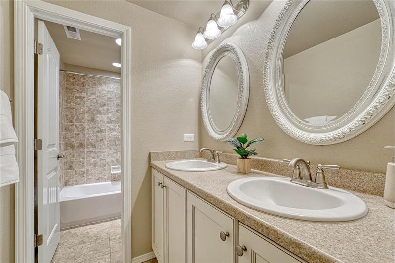 Basement Full Bathroom with dual sink vanity, framed mirrors, and tiled tub/shower.
