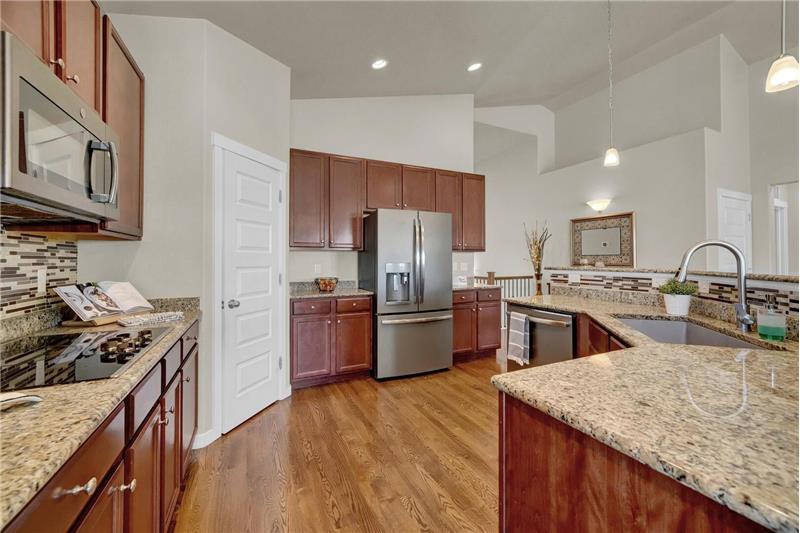 The Gourmet Kitchen features a counter bar w/pendant lights & bar stools, & 42’cabinets w/granite countertops & tile backsplash