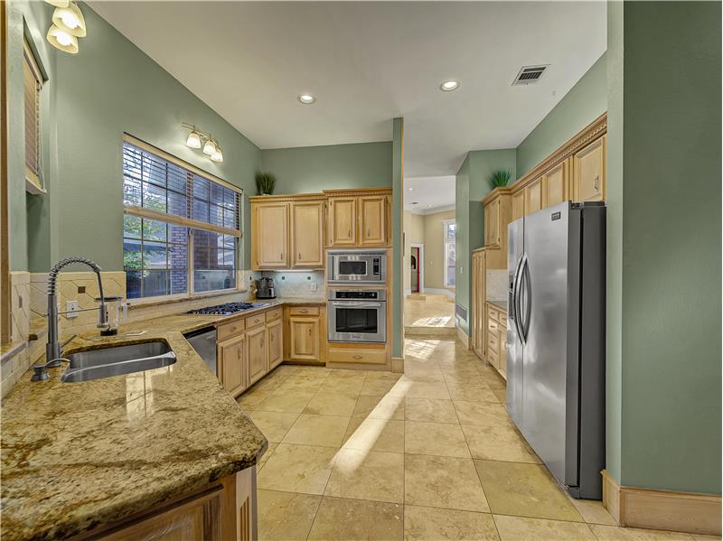 Kitchen with light brown wood cabinets, Granite countertops, appliances with stainless steel finishes, and decorative backsplash