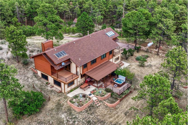Aerial rear view of home, yard, and surrounding treed lot.