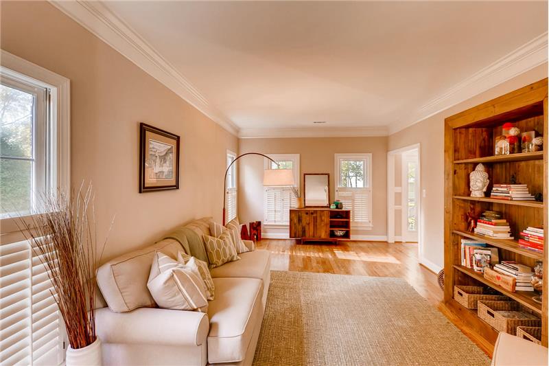 Large, sunny, open living room with hardwood floors, crown molding, plantation shutters.