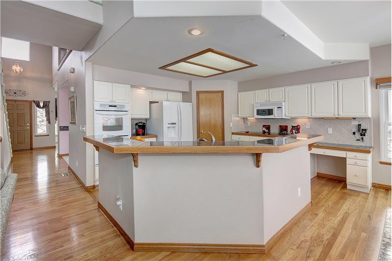 Open kitchen with convection double ovens, electric cooktop, overhead microwave, and kitchen desk