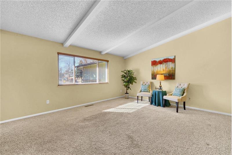 The spacious, vaulted Living Room has beamed ceilings, neutral carpet, and a large window to bring in natural light.