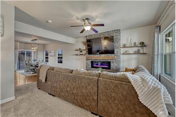 The Living Room features neutral carpet, a lighted ceiling fan, and electric fireplace with floor to ceiling stone surround.