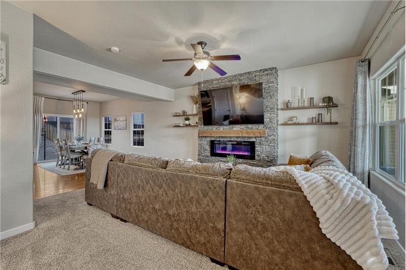 The Living Room features neutral carpet, a lighted ceiling fan, and electric fireplace with floor to ceiling stone surround.
