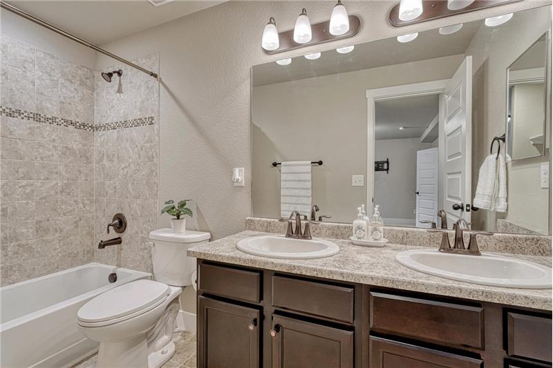 Basement Full Bathroom with dual sink vanity, mirror, and tiled tub/shower.