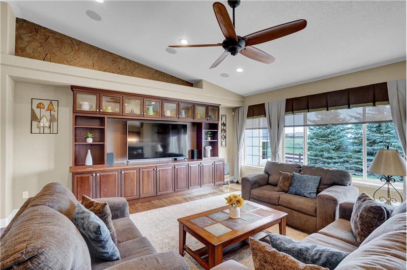 Vaulted Great Rm has recessed lights, a ceiling fan, wall of windows, built-in entertainment center, & dual sided gas-log FP