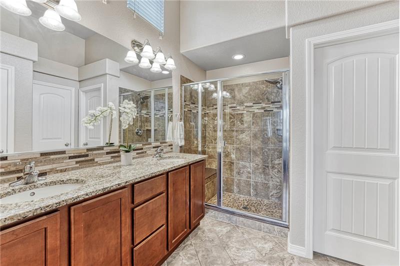 Luxurious primary bath with comfort height counters, dual sink vanity with undermount sinks, and tile backsplash. Tiled shower a