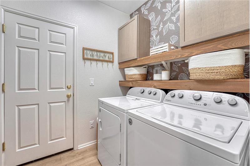 The Laundry Room has garage access and features wood shelving, upper cabinets, and washer and dryer that stay.