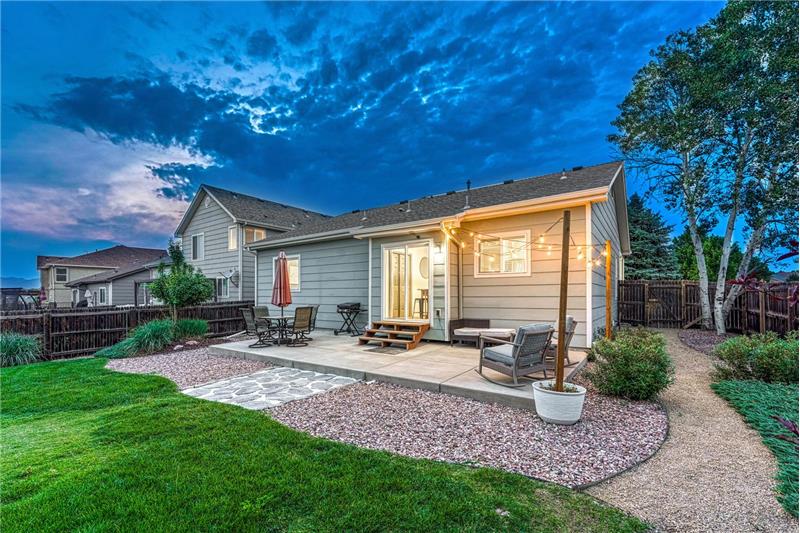 Sunset view of the backyard patio and grass areas with trees and shrubs.