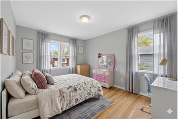 Bright bedroom featuring light wood-finish flooring, light grey walls, and multiple windows