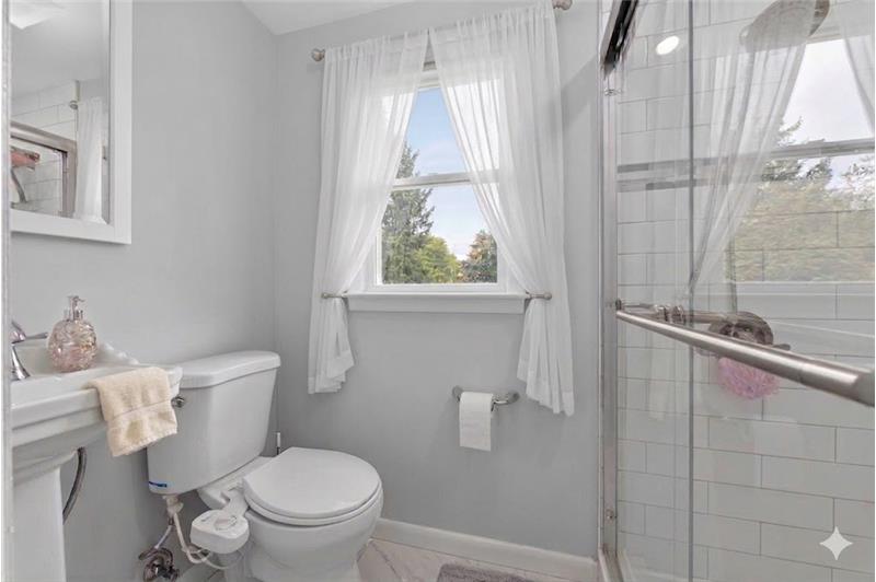 Bathroom featuring a glass-enclosed shower with white subway tile, a white pedestal sink