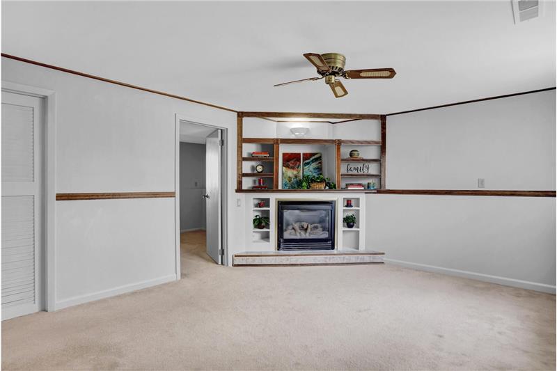 Lower-level Family Room with neutral carpet, ceiling fan, gas-log fireplace and built-in shelves/entertainment center