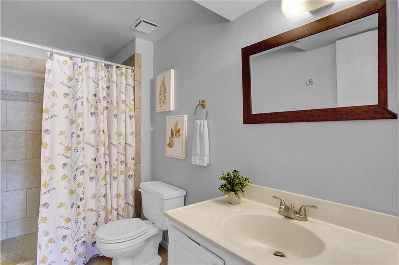 Lower-level shower bathroom with tile floors, vanity, framed mirror, and tiled shower with tile set shower pan