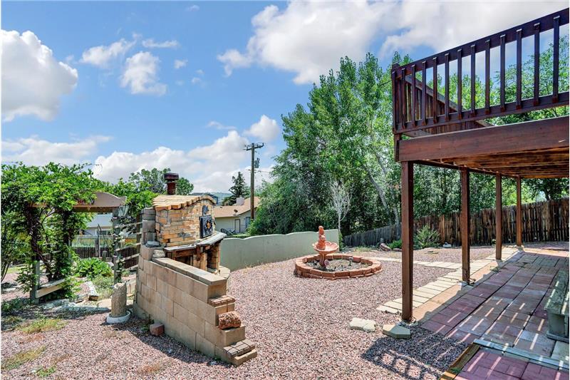 The backyard features a covered paver patio and a wood oven with a stone surround