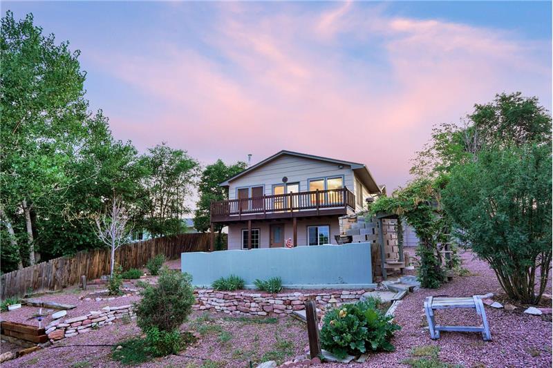 Sunset views of the fenced backyard with brick retaining walls, rock gardens, shrubs, and trees