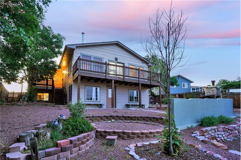 Sunset views of the backyard with covered paver patio, upper deck, upper side landing w/stairs to the backyard, & door to studio