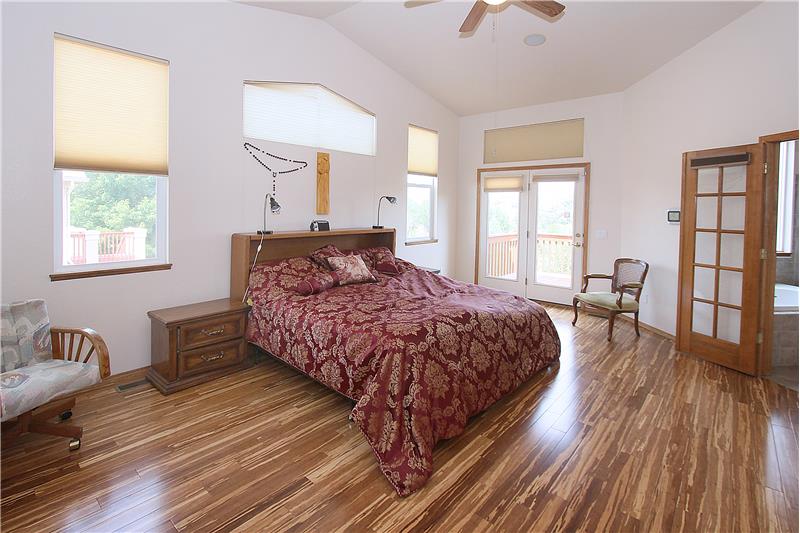 Large master bedroom with bamboo flooring, vaulted ceilings, in-ceiling speakers, and walk out to deck