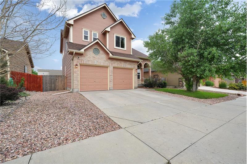 Low maintenance front yard with rock gardens, lush green grass, and large shade tree