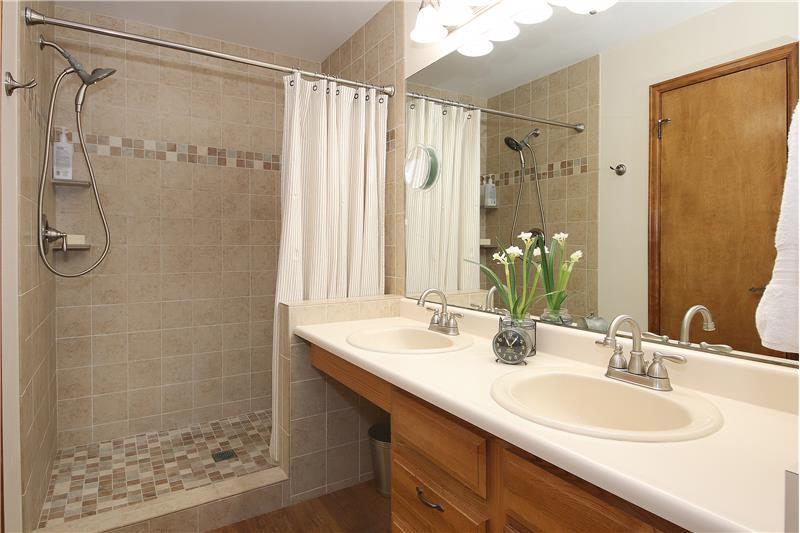 Master bathroom with double sink vanity, tile shower, walk-in closet, linen closet, and updated flooring