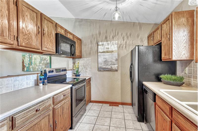Beautiful kitchen with tile floor, pendant lights, and updated appliances including a dishwasher, smooth top range oven, built-i