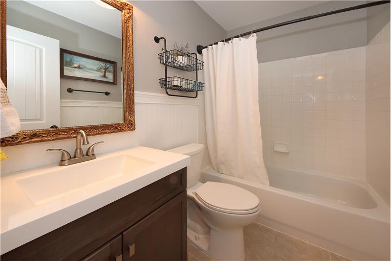 The full Hall Bathroom has a tile floor, vanity, framed mirror, wainscoting, & tub/shower