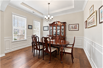 Elegant formal dining room with wide plank hardwood floors, tray ceiling, crown molding and detailed picture-frame wainscoting.