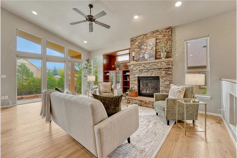 Vaulted Great Room with wood floor, wall of windows, gas fireplace with stacked stone surround and built-ins.