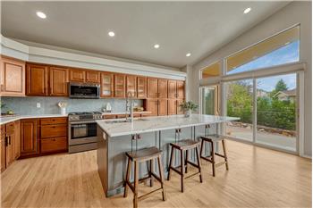The Gourmet Kitchen features an island, breakfast bar, wood cabinetry, quartz countertops, & black stainless steel appliances.