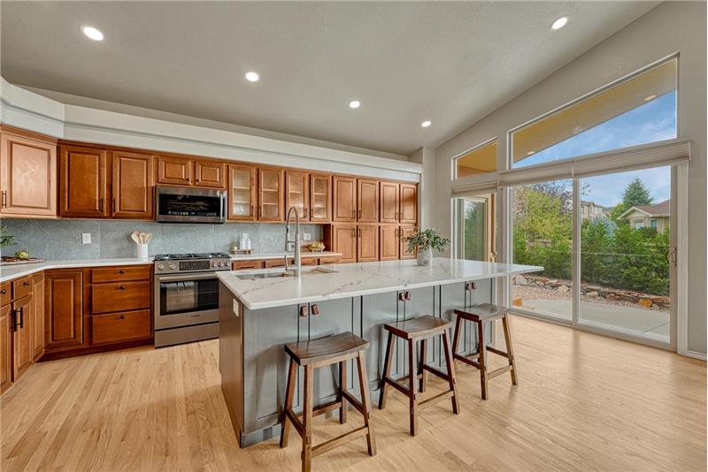 The Gourmet Kitchen features an island, breakfast bar, wood cabinetry, quartz countertops, & black stainless steel appliances.