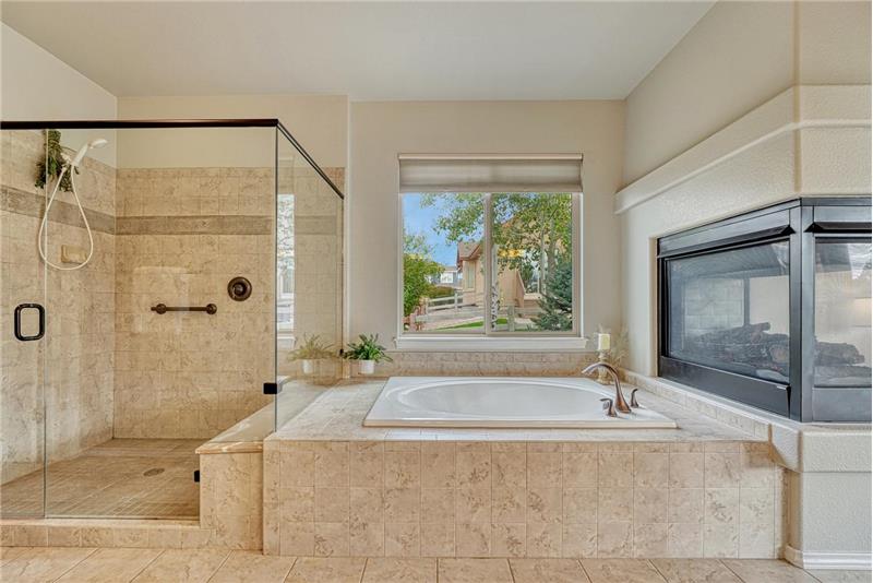 Luxurious 5-piece Primary Bathroom with 3-sided fireplace, soaking tub, and separate large tiled shower with built-in bench.