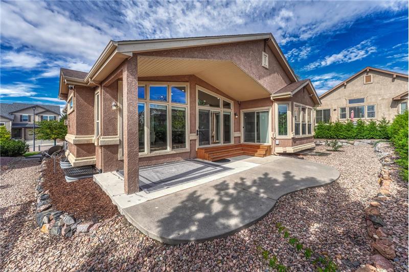 Low maintenance xeriscaped backyard yard with partially covered patio and many trees for privacy and shade.
