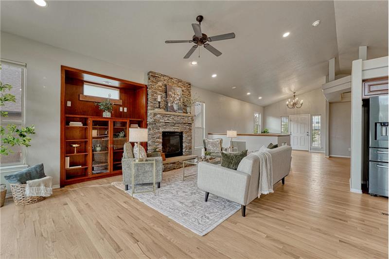 The spacious Great Room features wood flooring, a ceiling fan, custom built-ins, and a a gas fireplace.