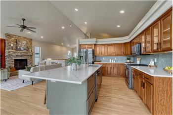 The gourmet island kitchen showcases quartz countertops, wood cabinetry, black stainless steel appliances, & New Gen lighting.