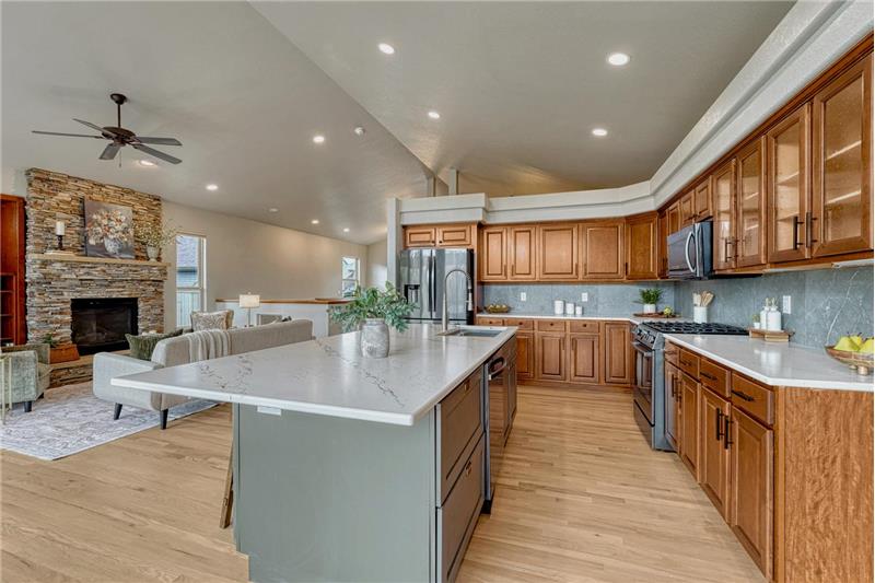 The gourmet island kitchen showcases quartz countertops, wood cabinetry, black stainless steel appliances, & New Gen lighting.