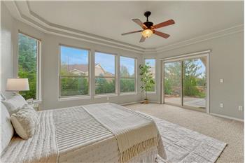 The main level Primary Bedroom features a tray ceiling, lighted ceiling fan, wall of windows, & slider to the back patio.