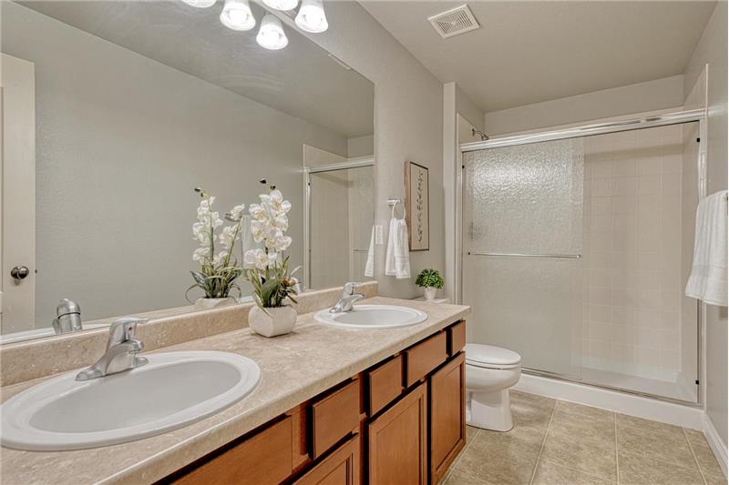 The Basement Shower Bathroom features vinyl flooring, a dual sink vanity, mirror, and enclosed shower.
