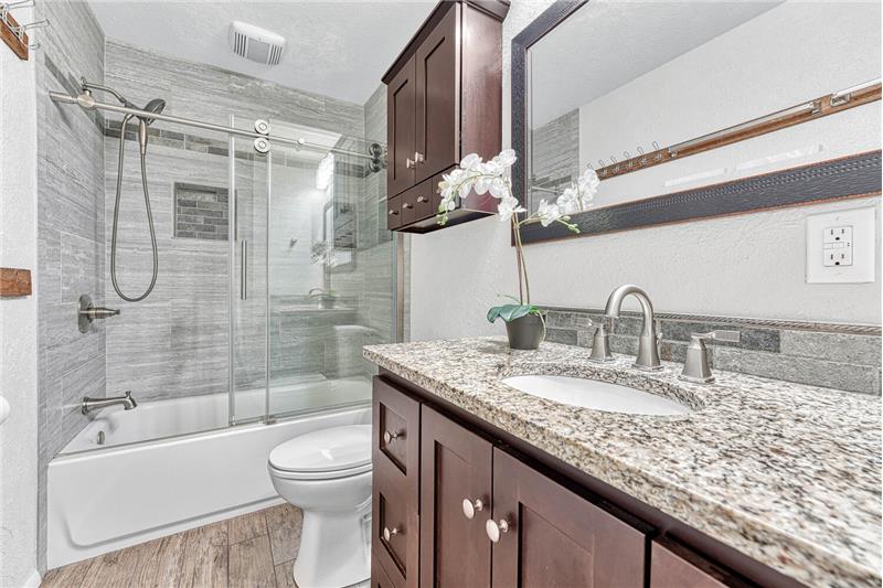 Upper level full bath redone w/new vanity, granite, new lighting, tiled tub surround w/built-in niches, & frameless door
