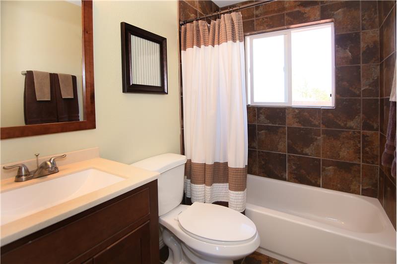 Updated main level full bath with tile surround, tile floor, and updated vanity.
