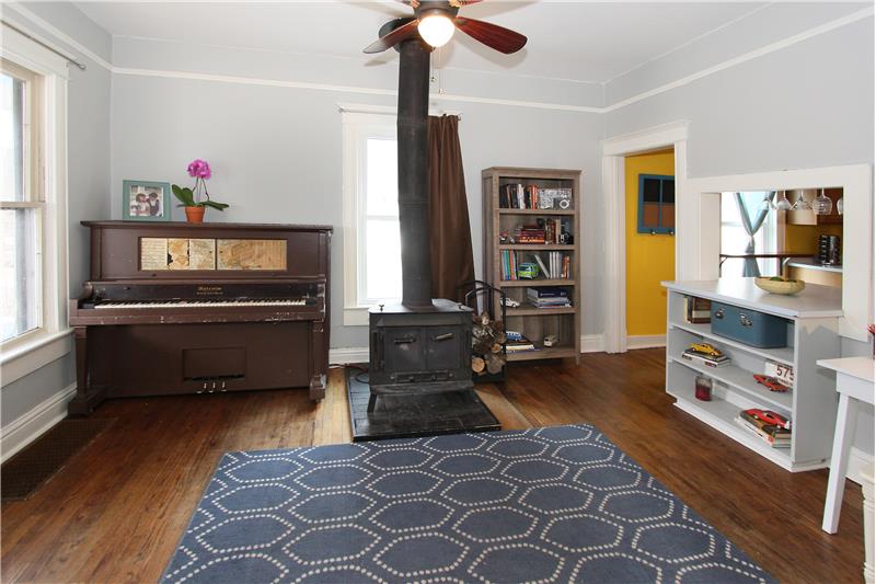 Living room with a wood burning stove, hardwood floors, built-in shelving, and ceiling fan.