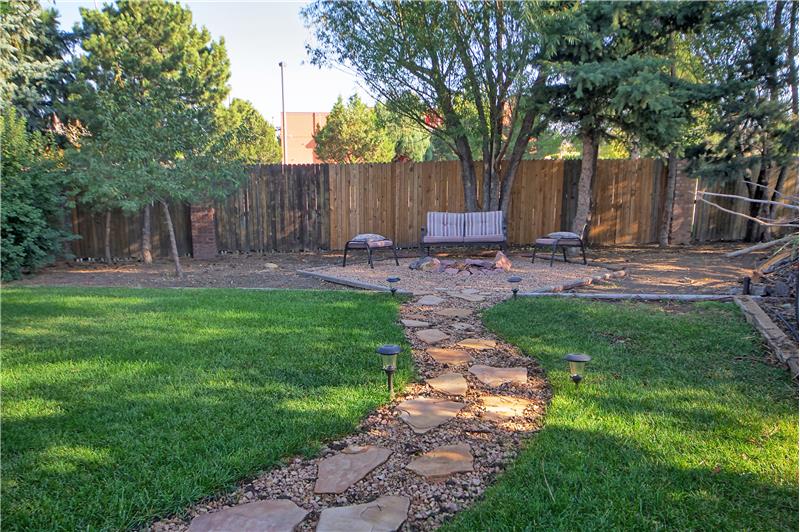 Backyard with flagstone patio, in-ground fire pit, garden, numerous trees, rose bushes, and large gate for trailer access.